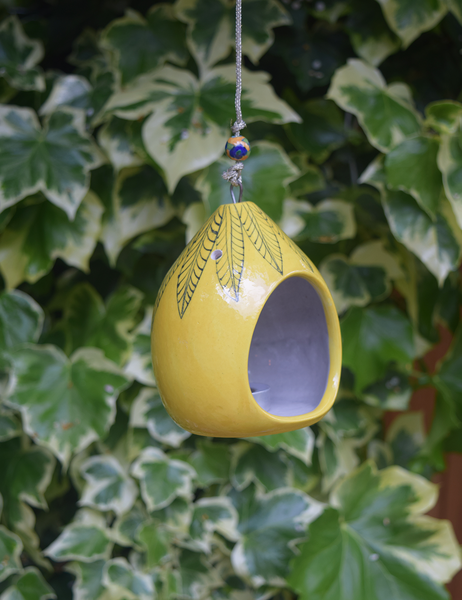 pictured in garden- yellow tealight holder with hand painted black leaf pattern, including a yellow and blue bead