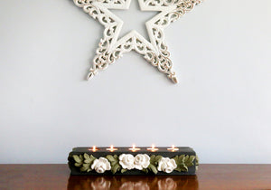 Charcoal tealight base with white roses and green leaves against a grey background with a white star