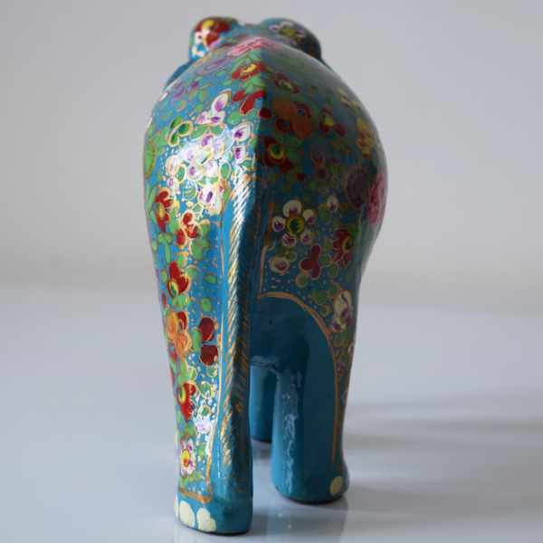Turquoise paper mache elephant with multicoloured flowers and green leaves on trunk and body- back view