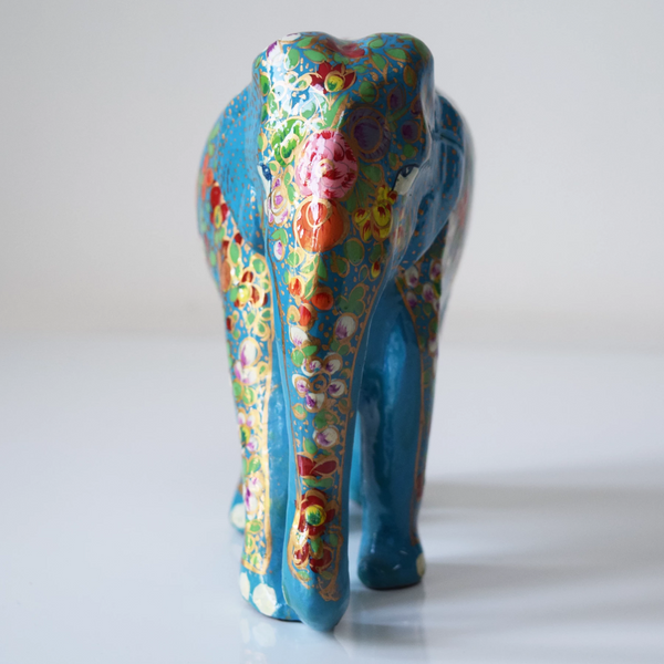 Turquoise paper mache elephant with multicoloured flowers and green leaves on trunk and body- front view
