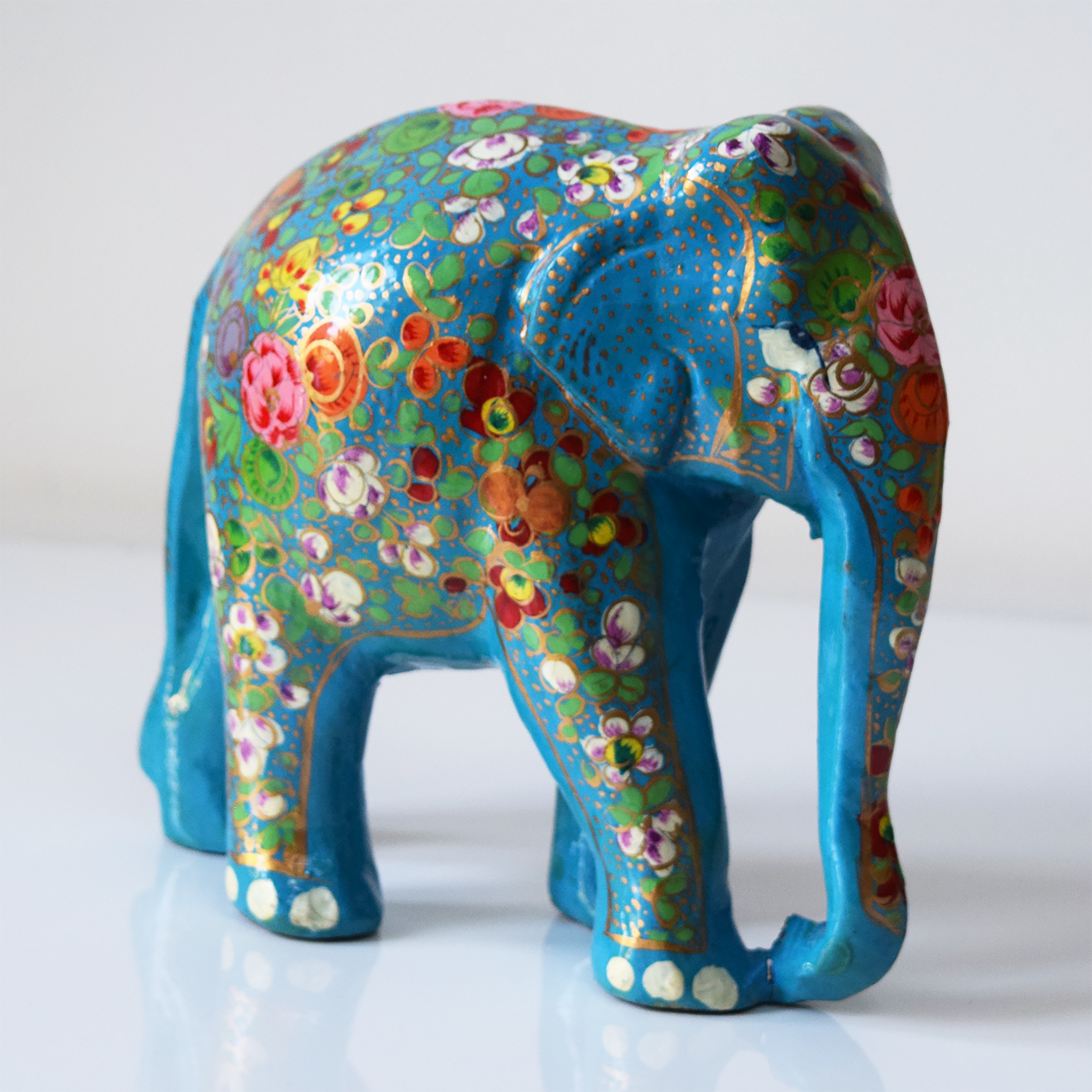 Turquoise paper mache elephant with multicoloured flowers and green leaves on trunk and body- side view