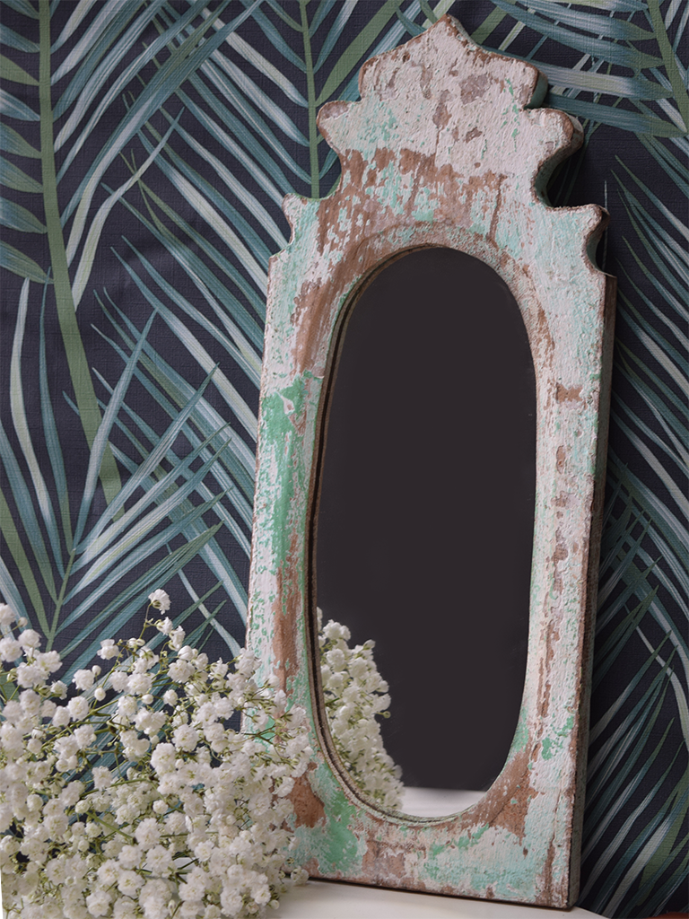 mint green distressed oval mirror against leafy wallpaper